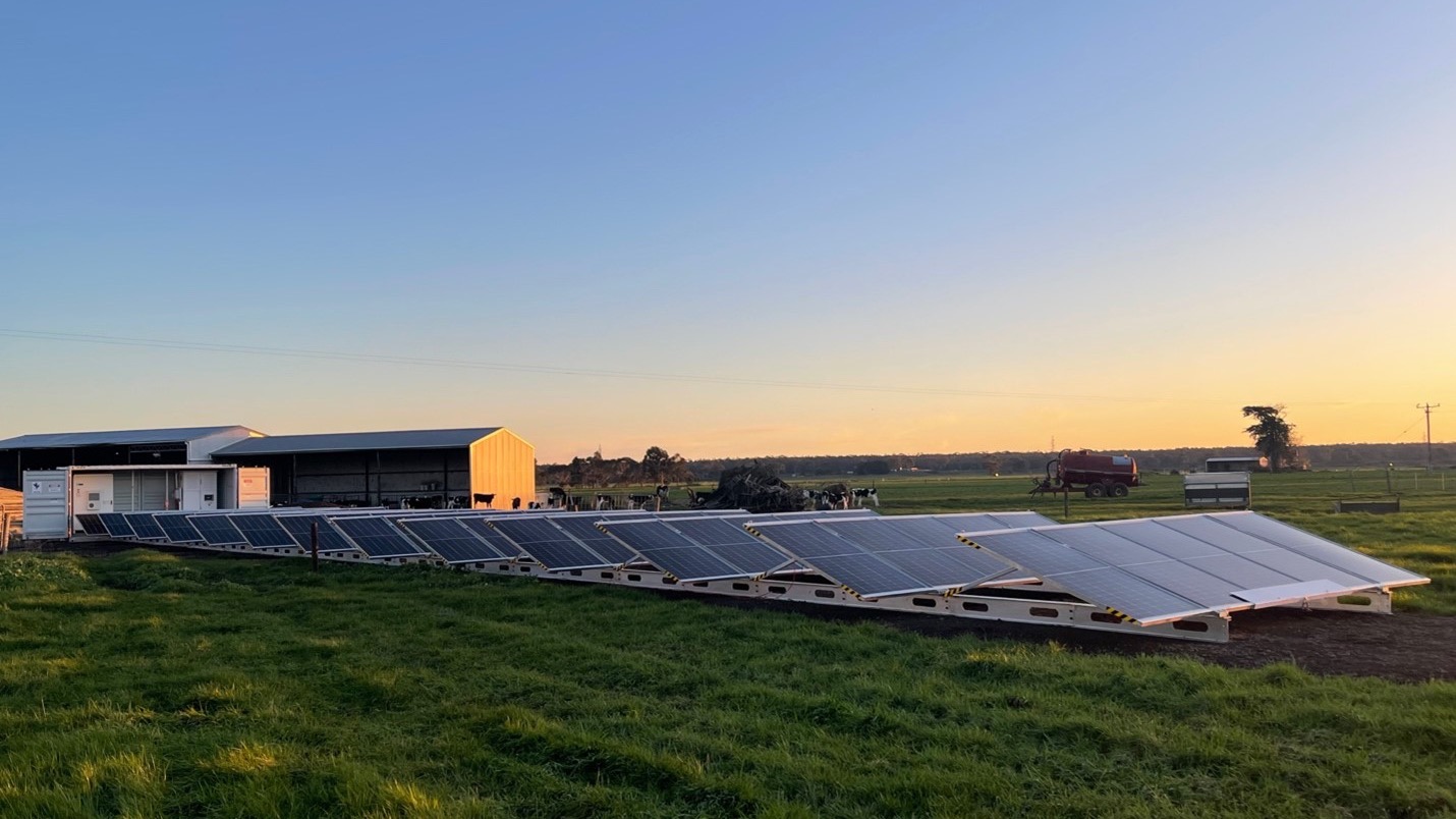 Seed Energy container with solar panels deployed beside a dairy barn at sunset